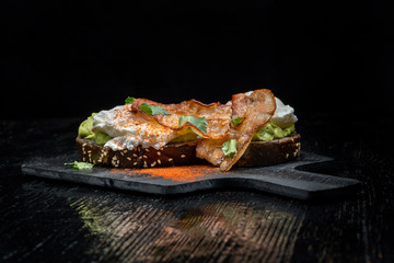 Poached eggs with bacon on toasts. Laid out on black slate.