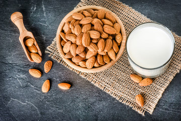 Almonds in bowl from top view. Almonds in wooden scoop. Almonds on jute with fresh milk on stone dark table.