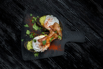 Poached eggs with bacon on toasts. Laid out on black slate.