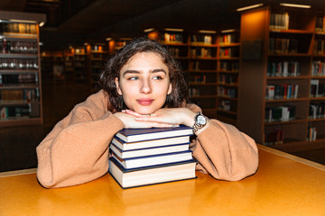Young woman holding stack of books in library