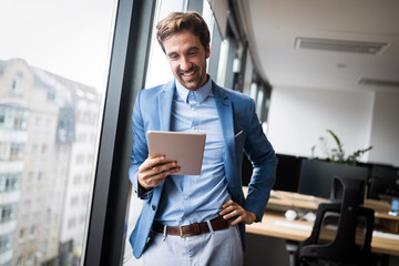 Portrait of young businessman smiling while using digital tablet in office - Powered by Adobe