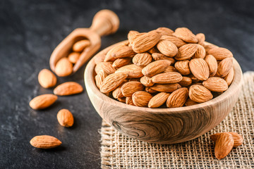 Almonds in bowl from top view. Almonds in wooden scoop. Almonds on jute on stone dark table.