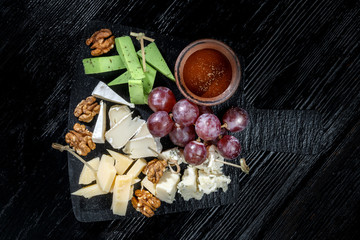 Plate with cheeses, grapes, walnuts. Laid out on black slate.