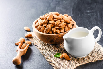 Fresh almonds in wooden bowl and full almond scoop on dark stone table. Almonds with jar of milk.