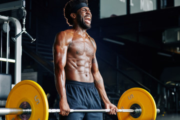 Fototapeta na wymiar Shirtless strong young sportsman shouting when lifting heavy weight in gym