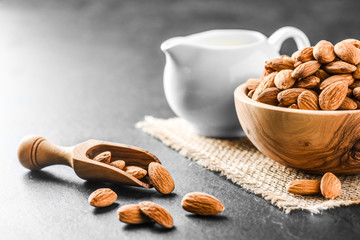 Almonds on dark stone table. Fresh peeled almonds in bowl. Almonds in scoop and milk in ceramic jar.