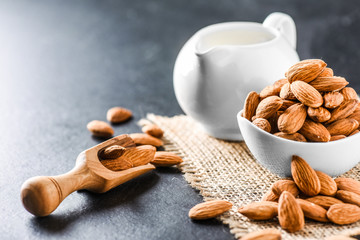 Almonds on dark stone table. Fresh peeled almonds in bowl. Almonds in scoop and milk in ceramic jar.