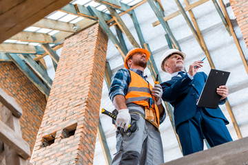 low angle view of bearded businessman holding clipboard near builder