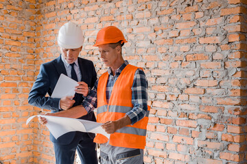 architect holding blueprint near businessman with digital tablet