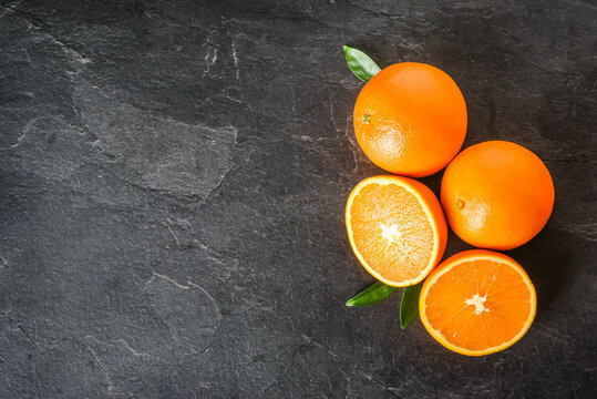 Fresh oranges on dark stone table. Half oranges on table from top view. Tasty oranges fruits. © Milan
