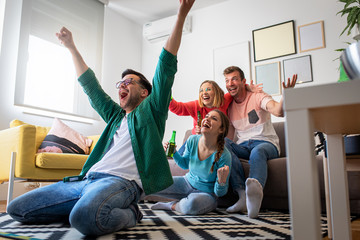 Group of cheerful friends watching soccer match and celebrating victory at home. Man on his knees...