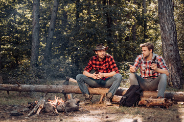 Good day for spring picnic in nature. Friends relaxing near campfire after day hiking or gathering mushrooms. Two Happy people sitting around campfire with beer.