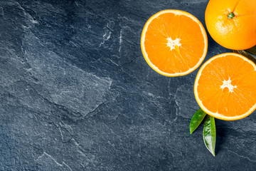 Oranges on dark stone table. Fresh orange fruits on table top view. Half oranges with green leaves.