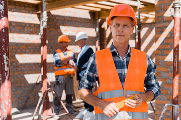 selective focus of mature man holding equipment while standing near coworker and businessman