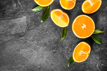 Oranges on dark stone table. Fresh orange fruits on table top view. Half oranges with green leaves.