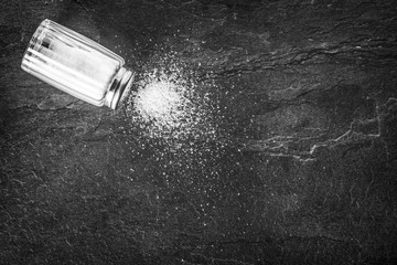 Salt. Glass salt shaker on dark stone table.  A pile of salt top view.