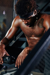 Tired muscular man resting on metal steps in gym with bottle of fresh water