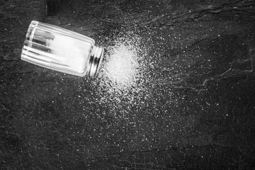 Naklejka na ściany i meble Salt shaker on black stone table. Sea salt on dark background.