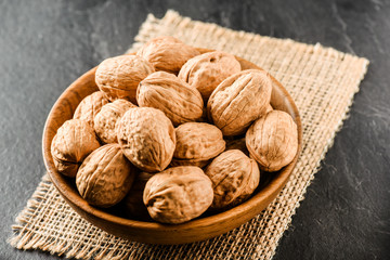 Walnuts in wooden bowl. Whole walnuts in vintage bowl on jute. Walnut kernel on black background.