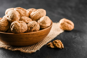 Walnuts in wooden bowl. Whole walnuts in vintage bowl on jute. Walnut kernel on black background.