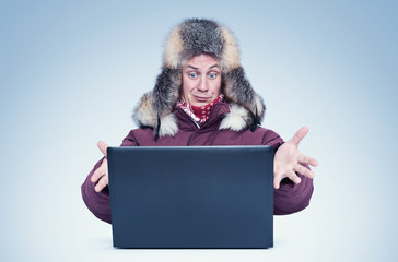 Frozen man in red winter clothes and a fur hat works at laptop in the cold. 