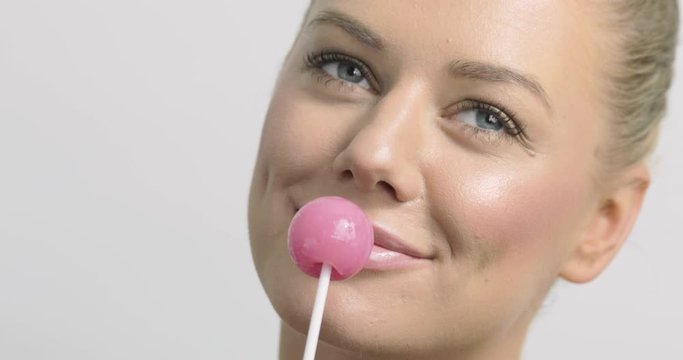 Close-up of a flirty and playful woman with a pink lollipop.