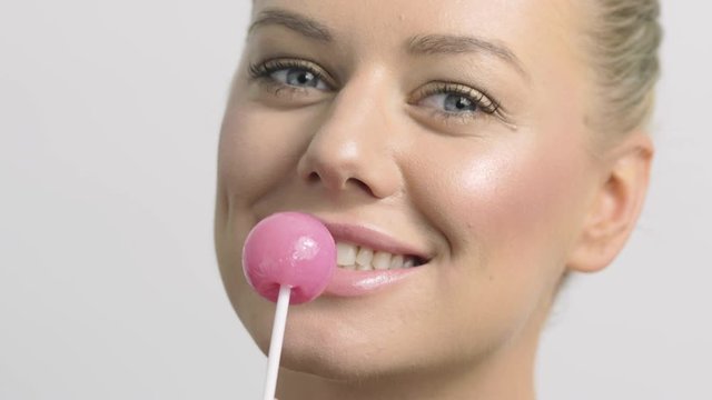 Sexy blonde woman with a lollipop smiles and pretends to bite.