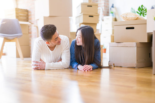 Young asian couple lying on the floor of new house arround cardboard boxes relaxing and smiling happy