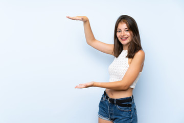 Young woman over isolated blue background holding copyspace to insert an ad