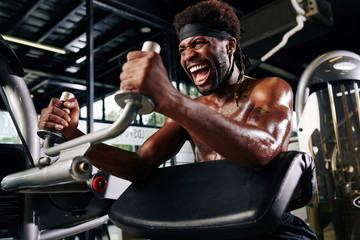 Fototapeta na wymiar Strong young man shouting to encourage himself when doing exercise in gym machine