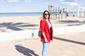Young beautiful woman walking down the promenade by the beach, smiling and enjoying a sunny day