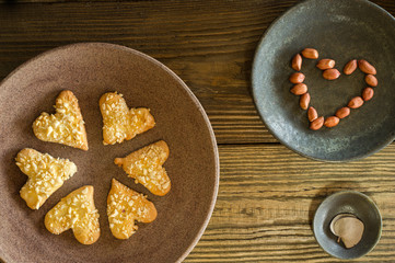 Shortbread cookies sprinkled with heart-shaped nut crumbs lie on a ceramic plate, next to peanuts laid out in the form of a heart and a Cup with a eucalyptus leaf, similar to a heart. Horizontal.