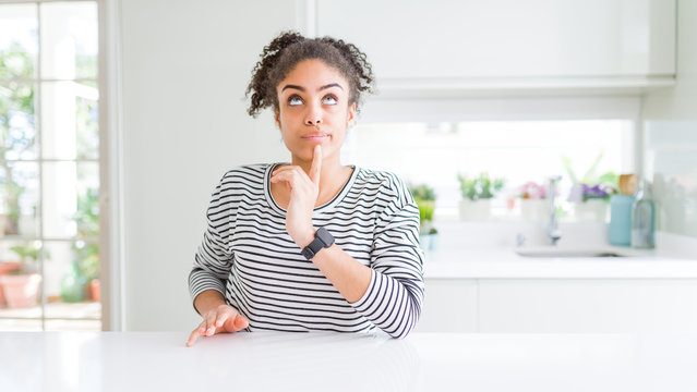 Beautiful african american woman with afro hair wearing casual striped sweater Thinking concentrated about doubt with finger on chin and looking up wondering