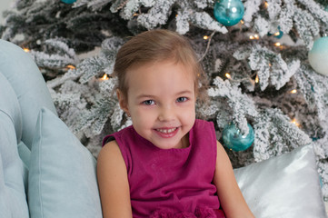 Smiling child girl near the Christmas tree in turquoise tones