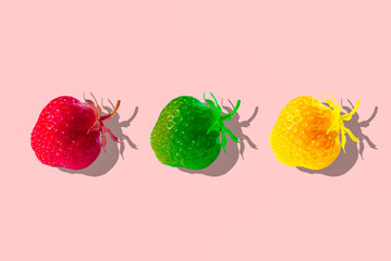 Creative still life, top view, three strawberries of different colors (red, yellow, green) in hard contrasting light with a sharp shadow on a pale pink background. Author's processing.