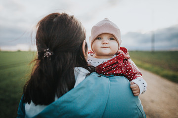 Infant baby looks over mothers shoulder - autumn outdoor family lifestyle concept