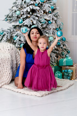 Young woman mother and little girl playing having fun with Christmas balls near the Christmas tree.