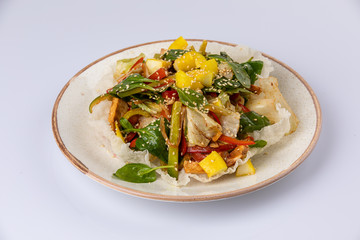 Salad with mango, spinach, bell pepper, sesame seeds lying on white plate.