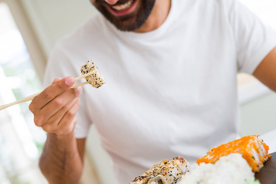 Handsome man smiling happy enjoying eating fresh colorful asian sushi using chopsticks