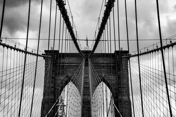 Obraz premium Brookyln Bridge Nowy Jork Manhattan czarno-biała grafika w skali szarości niebo chmury inżynier budowlany East River widok punkt orientacyjny kable podwieszane statyka łuki filary pilon murowane symetria