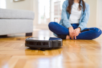 Young woman using automatic vacuum cleaner to clean the floor, controling machine housework robot