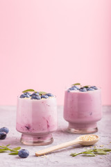 Obraz na płótnie Canvas Yoghurt with blueberry and sesame in a glass and wooden spoon on gray and pink background. side view.