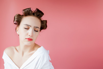 Beautiful young girl with a mask and curlers touching her face.