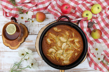 Pie with Apple on the wooden white background with a red tablecloth and flowers of cosmos. The concept of home food, healthy nutrition, comfort, warmth. Rustic style of life.