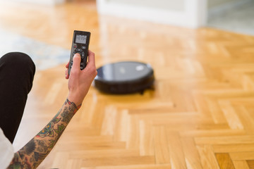 Close up of man hands controling automatic vacuum cleaner using electronic control of the mopping...