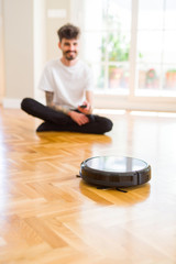 Young man using automatic vacuum cleaner to clean the floor, controling machine housework robot