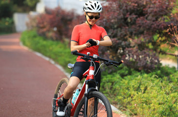 Woman cyclist looking at her smartwatch while riding bike outdoors on sunny day