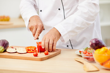 Close up of unrecognizable professional chef cutting vegetables while cooking delicious food in restaurant kitchen, copy space