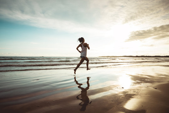 Fitness woman runner running on sunset beach