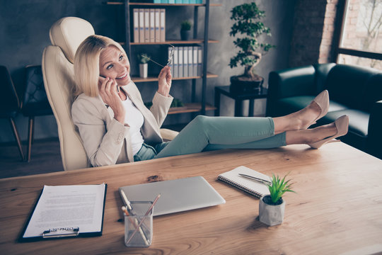 Photo Of Cheerful Nice Charming Positive Assistant Talking On Phone At The End Of Work Day Putting Her Eyewear Off With Legs On Table